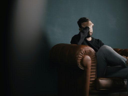 a man holds his head while sitting on a sofa