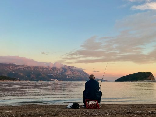 man in black jacket sitting on red and white fishing rod during daytime